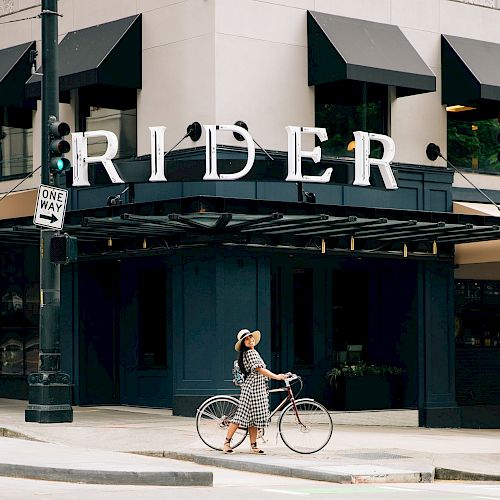 A person walks their bike on a city street in front of a building with the large sign 